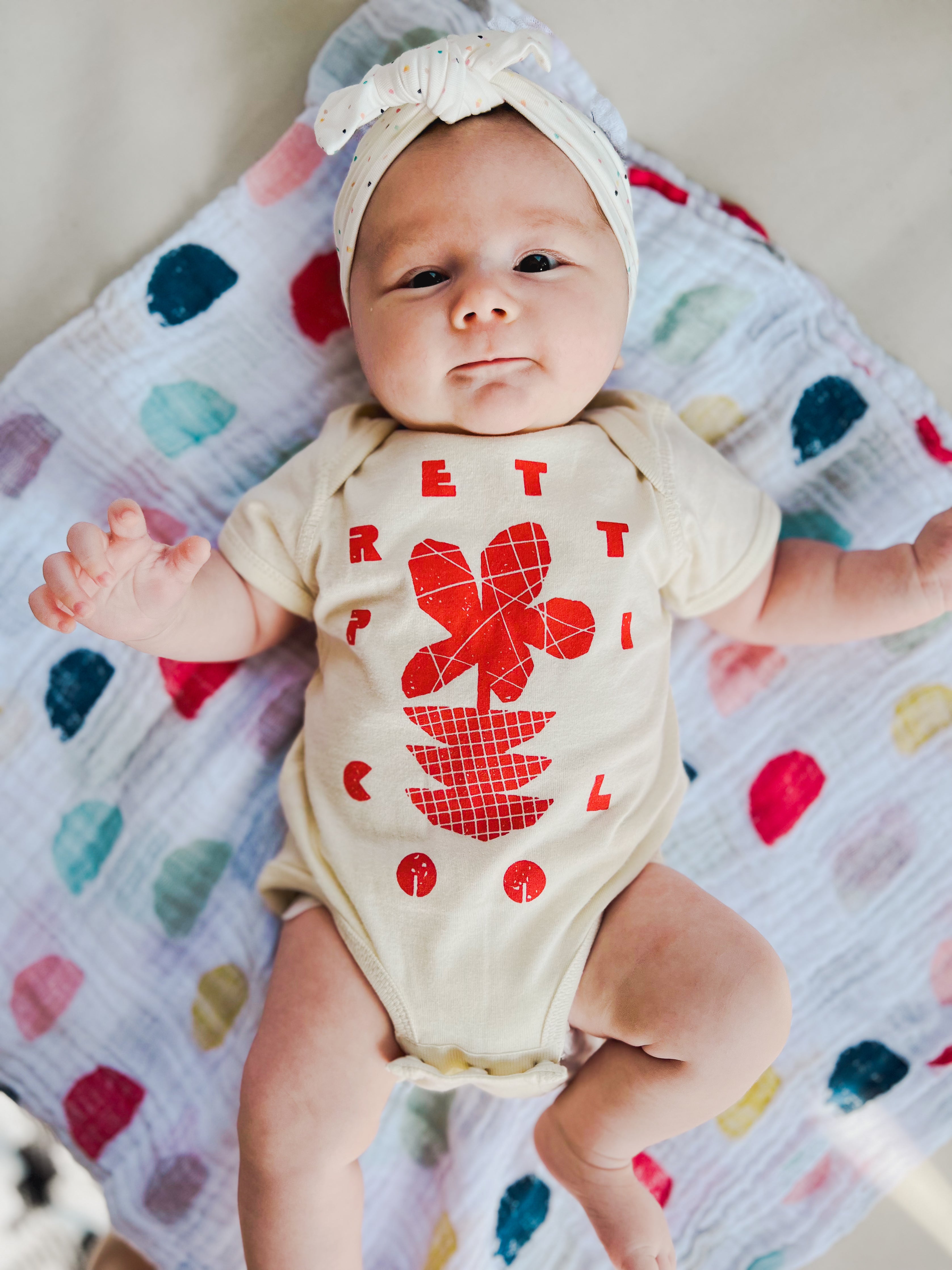 Flowers Onesie on Charli in Cream w/ Red/Orange.