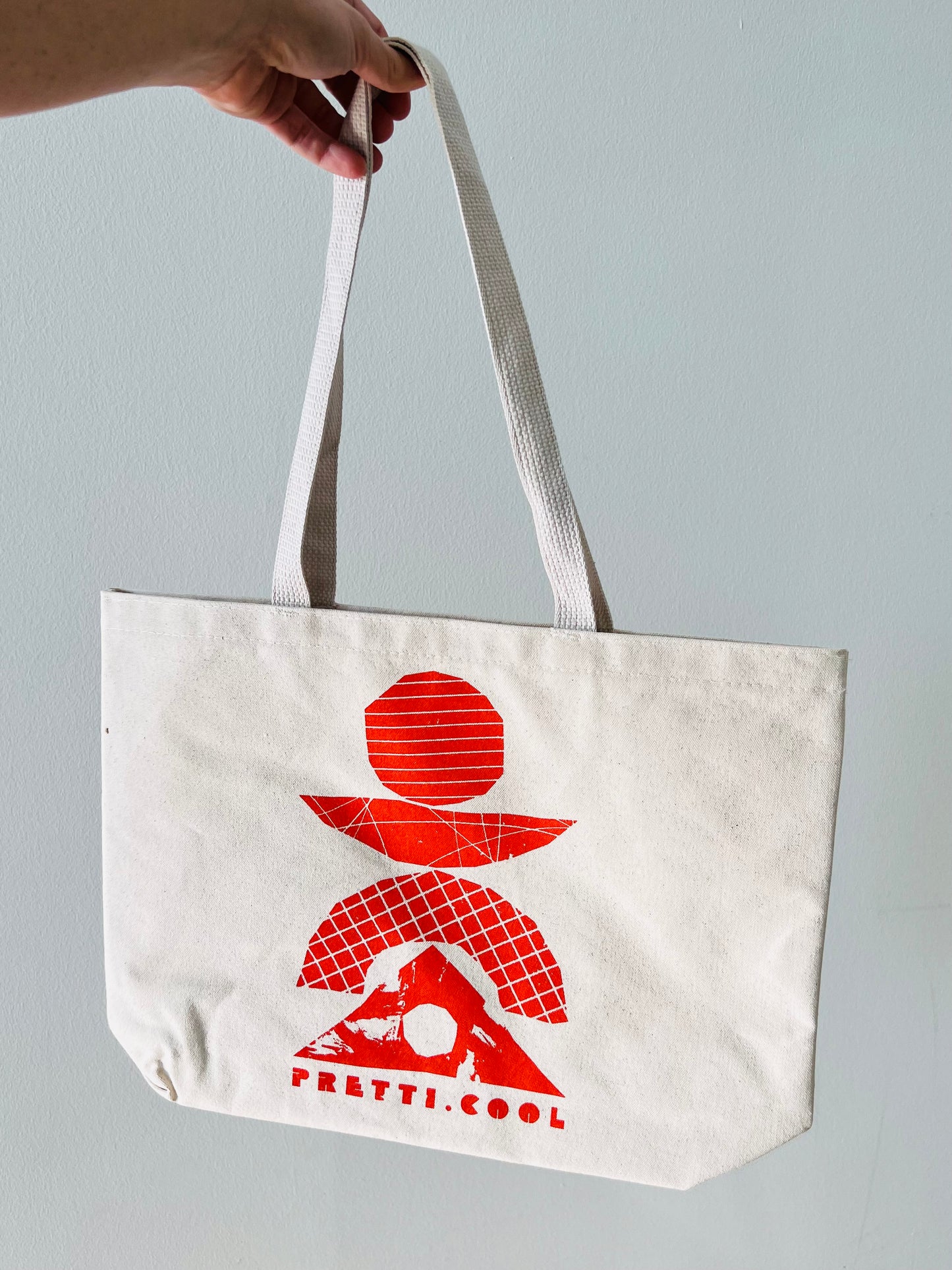 The pretti.cool tote in natural canvas w/ a red/orange print on the front.