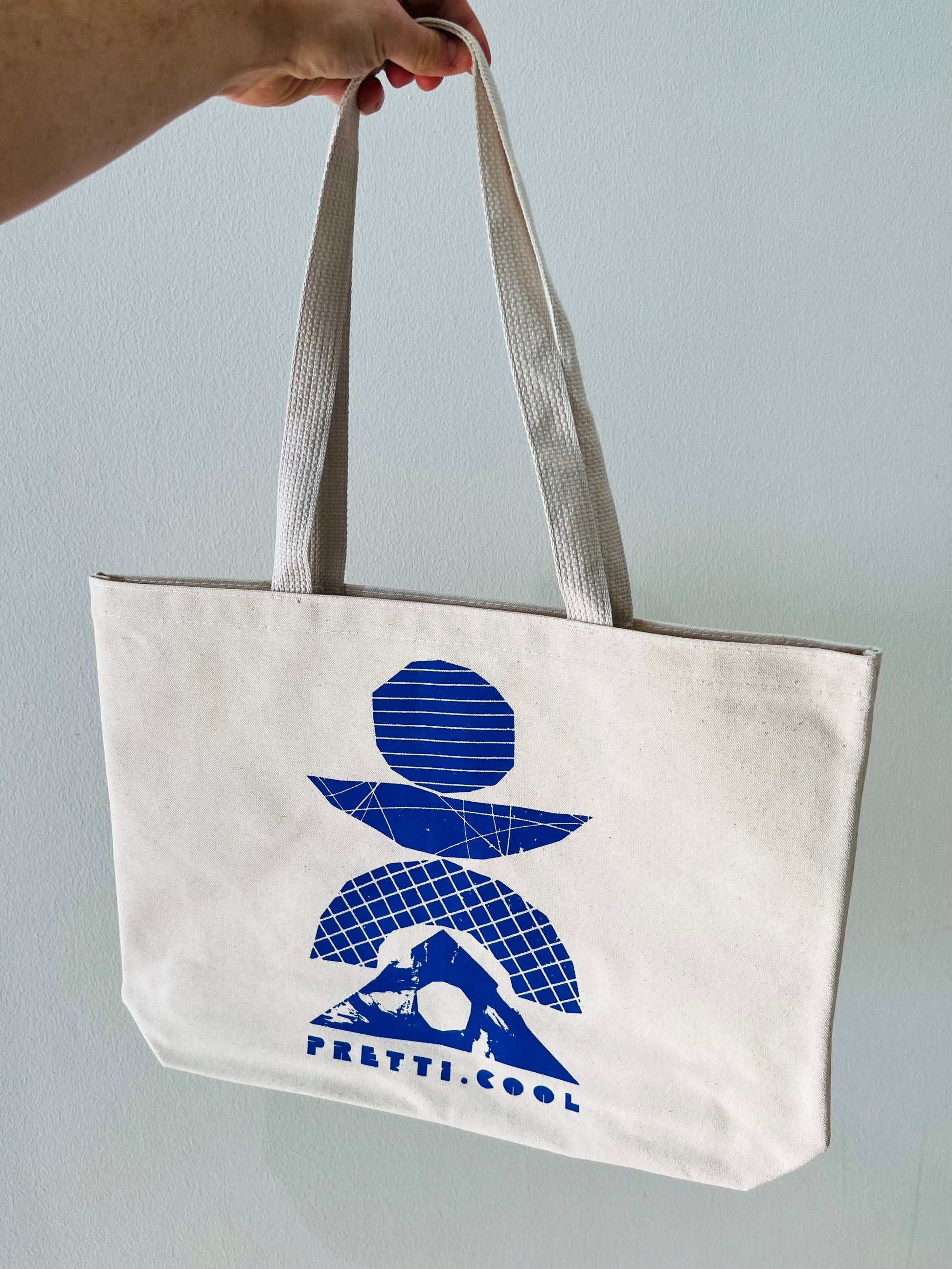 The pretti.cool tote in natural canvas w/ a cobalt print on the front.