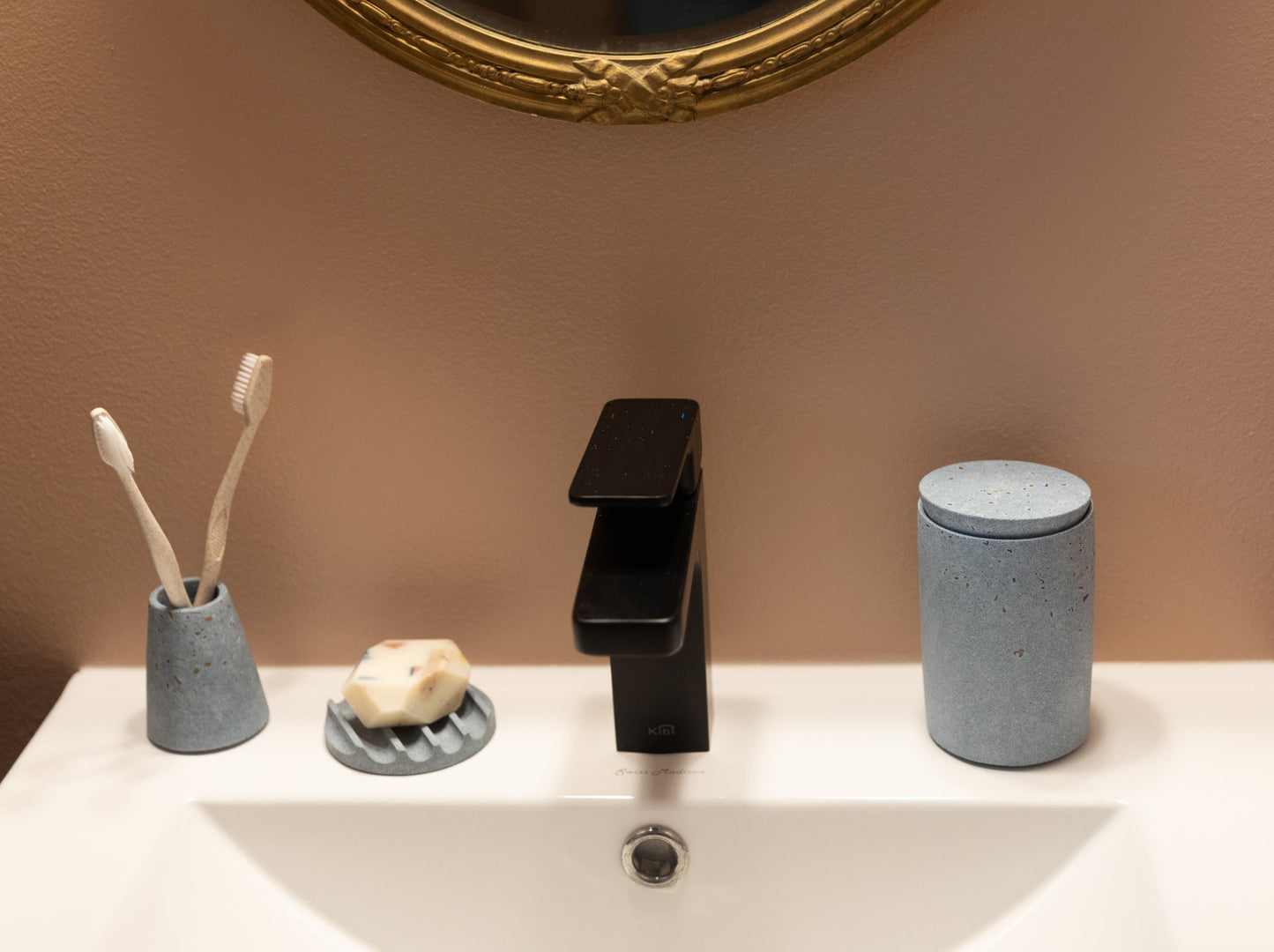Cotton swab holder, paired with a toothbrush holder and mini soap dish, all in light blue terrazzo, styled by a sink.