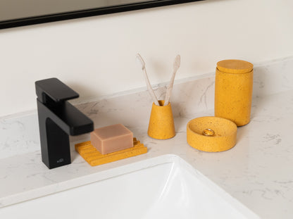 Cotton swab holder, paired with a toothbrush holder and soap dish, all in marigold terrazzo, styled by a sink.