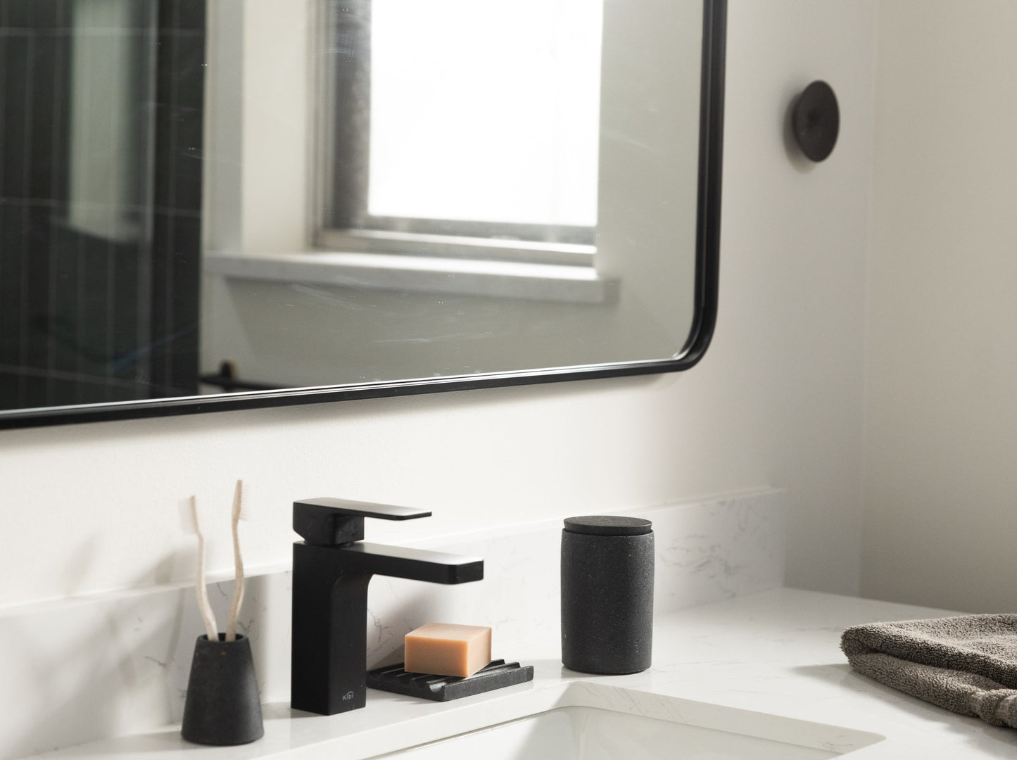 Cotton swab holder, paired with a toothbrush holder and soap dish, all in black terrazzo, styled by a sink.