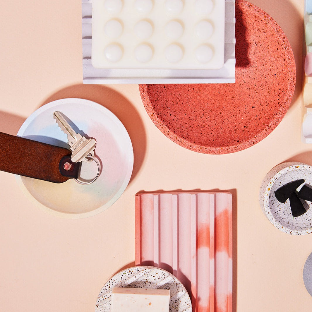 A 4" catch all in jawbreaker, 5" catch all in coral terrazzo, grey & white soap dish, pink & coral soap dish, mini white terrazzo soap dish, and white terrazzo incense holder, styled with various objects for scale.