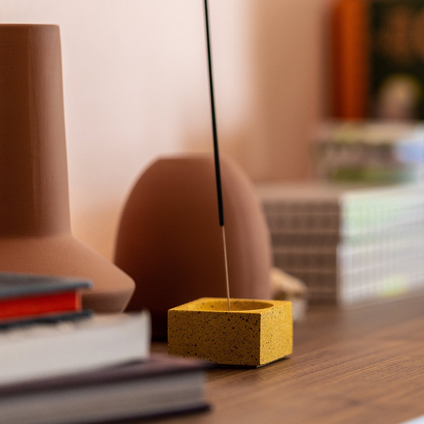 Square concrete terrazzo incense holder in marigold on desk with incense stick.