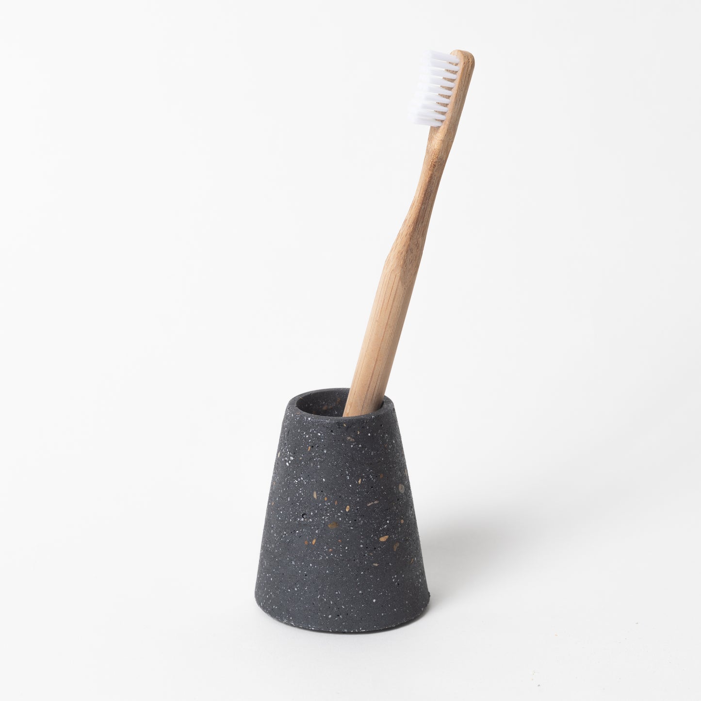 Concrete terrazzo toothbrush holder seen in black terrazzo holding toothbrush.