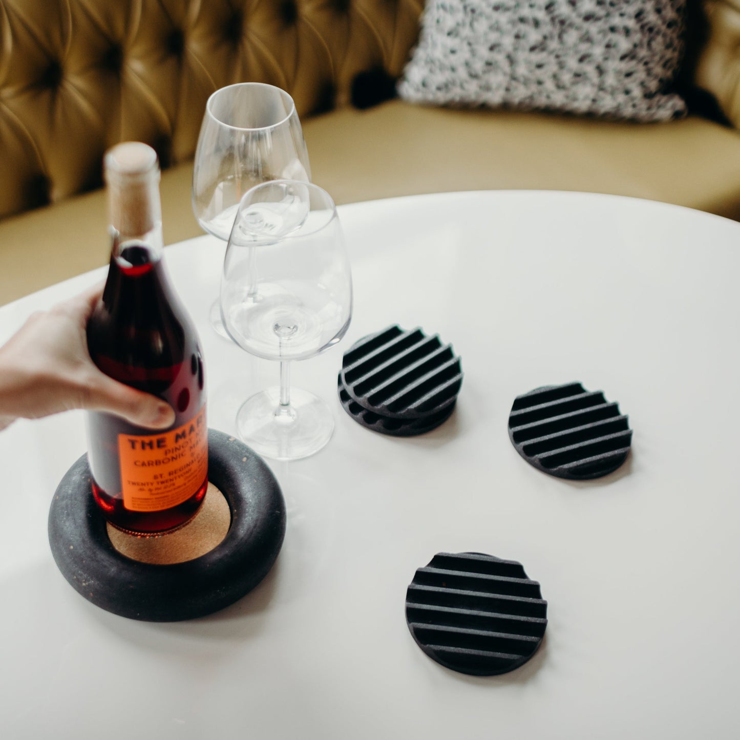 Concrete terrazzo coaster set in black with a black terrazzo wine coaster, wine bottle, and glasses.