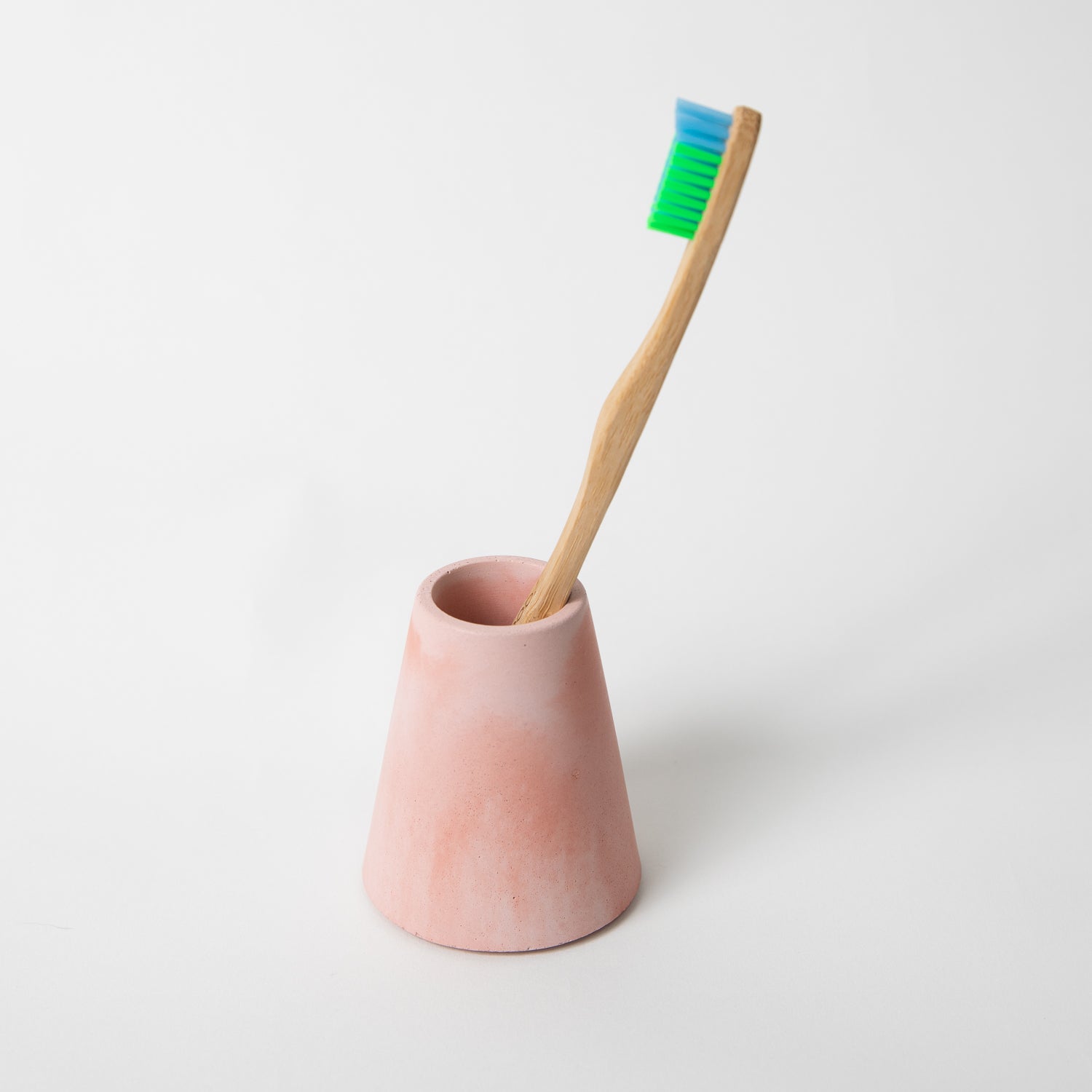 Concrete terrazzo toothbrush holder seen in pink and coral holding toothbrush.