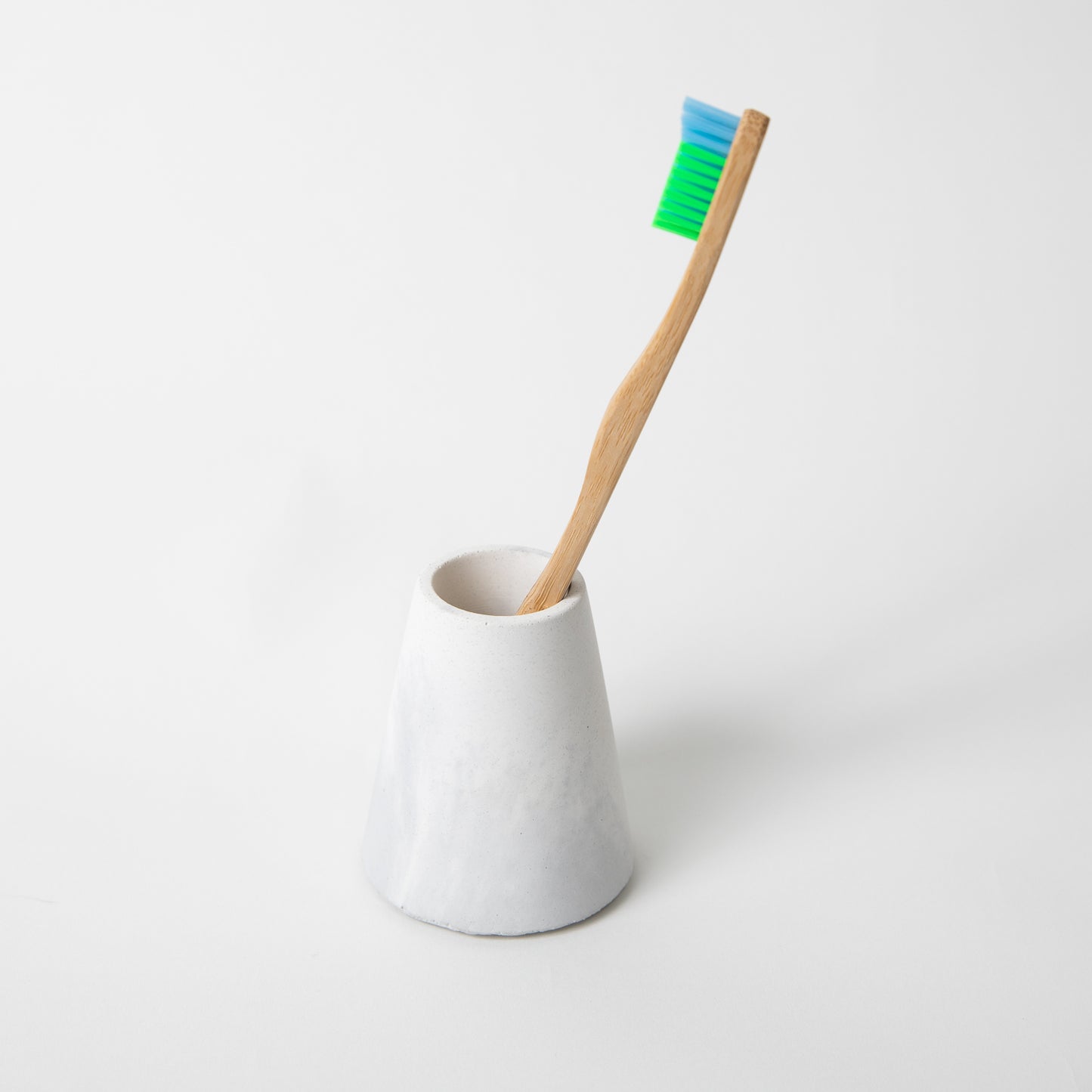 Concrete terrazzo toothbrush holder seen in grey and white with toothbrush.