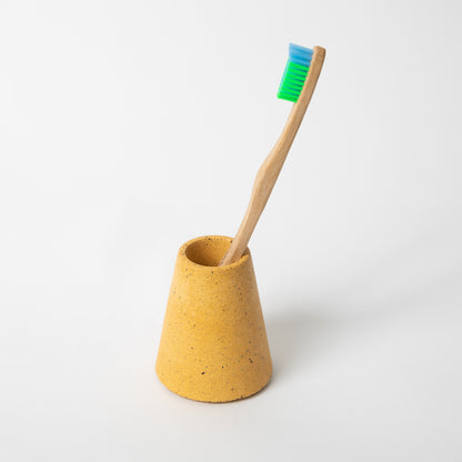 Concrete terrazzo toothbrush holder seen in marigold terrazzo with toothbrush.