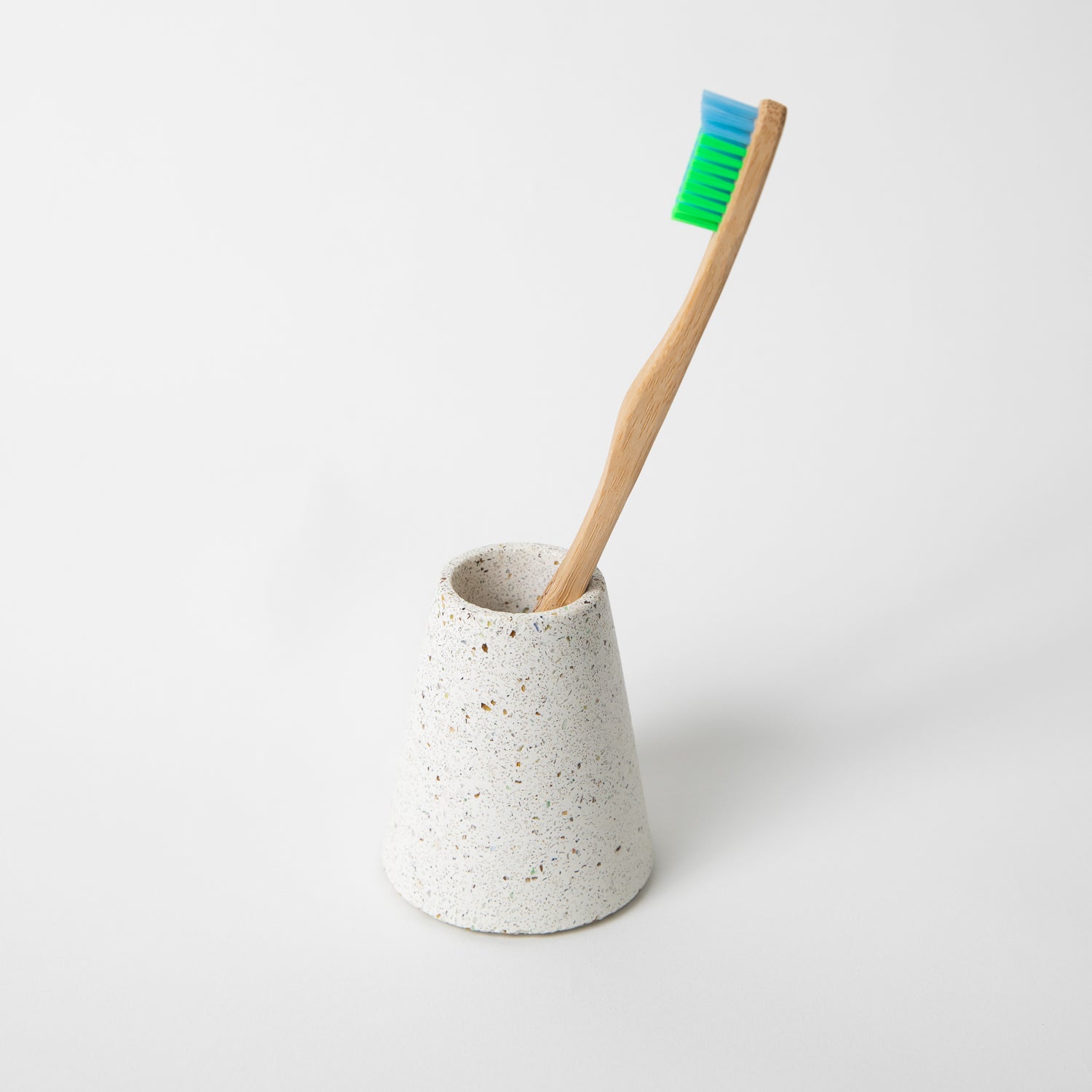 Concrete terrazzo toothbrush holder seen in white terrazzo with toothbrush.