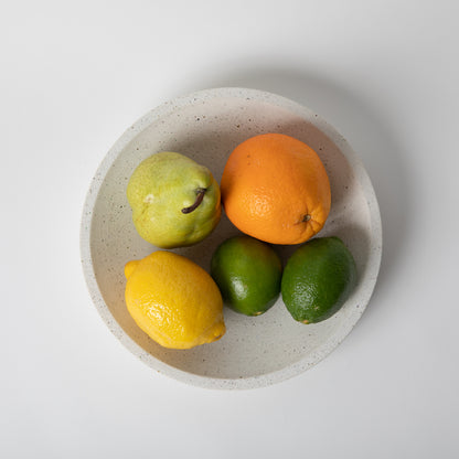 Large concrete centerpiece bowl in white terrazzo holding fruit from above angle.