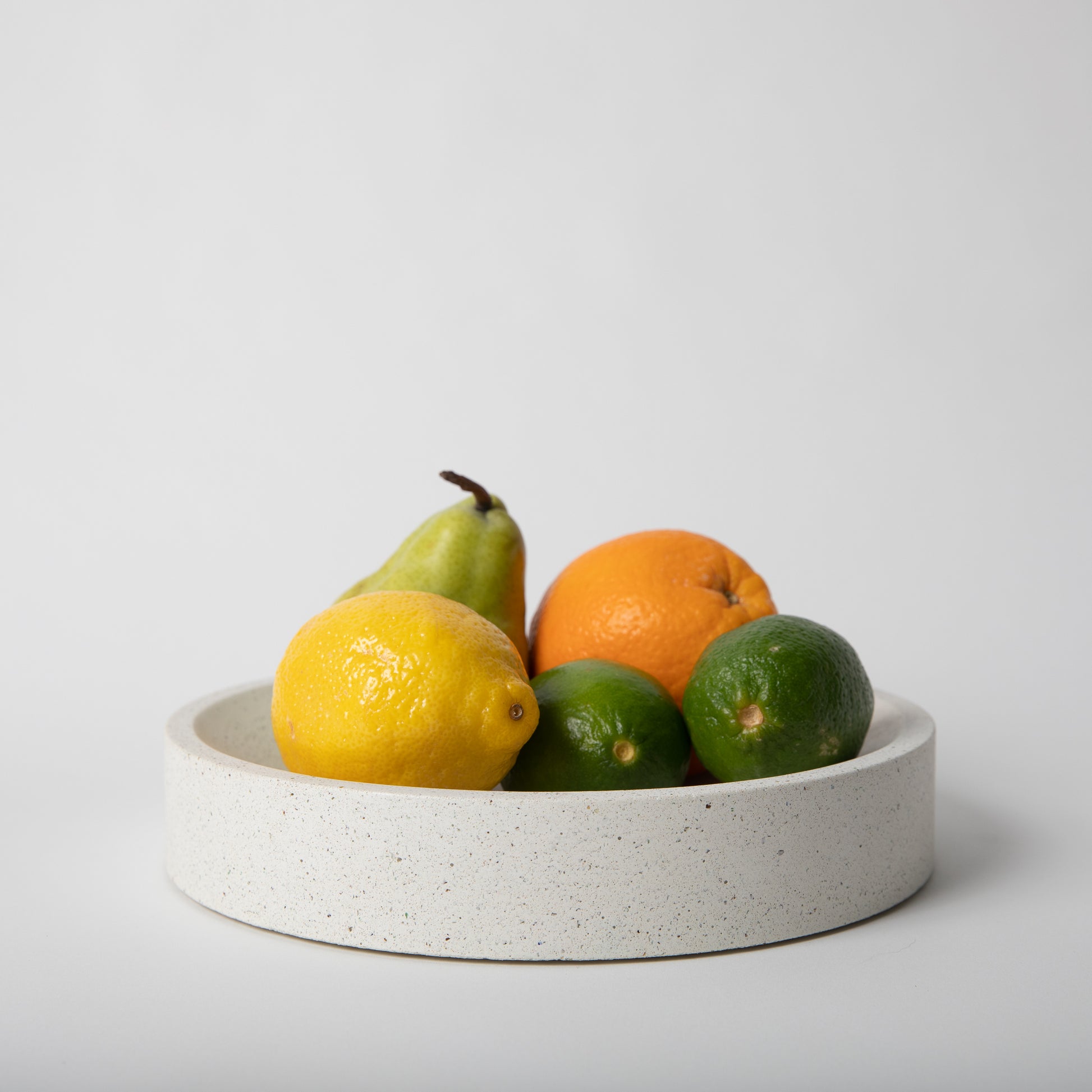 Large concrete centerpiece bowl in white terrazzo holding fruit in decorative way.