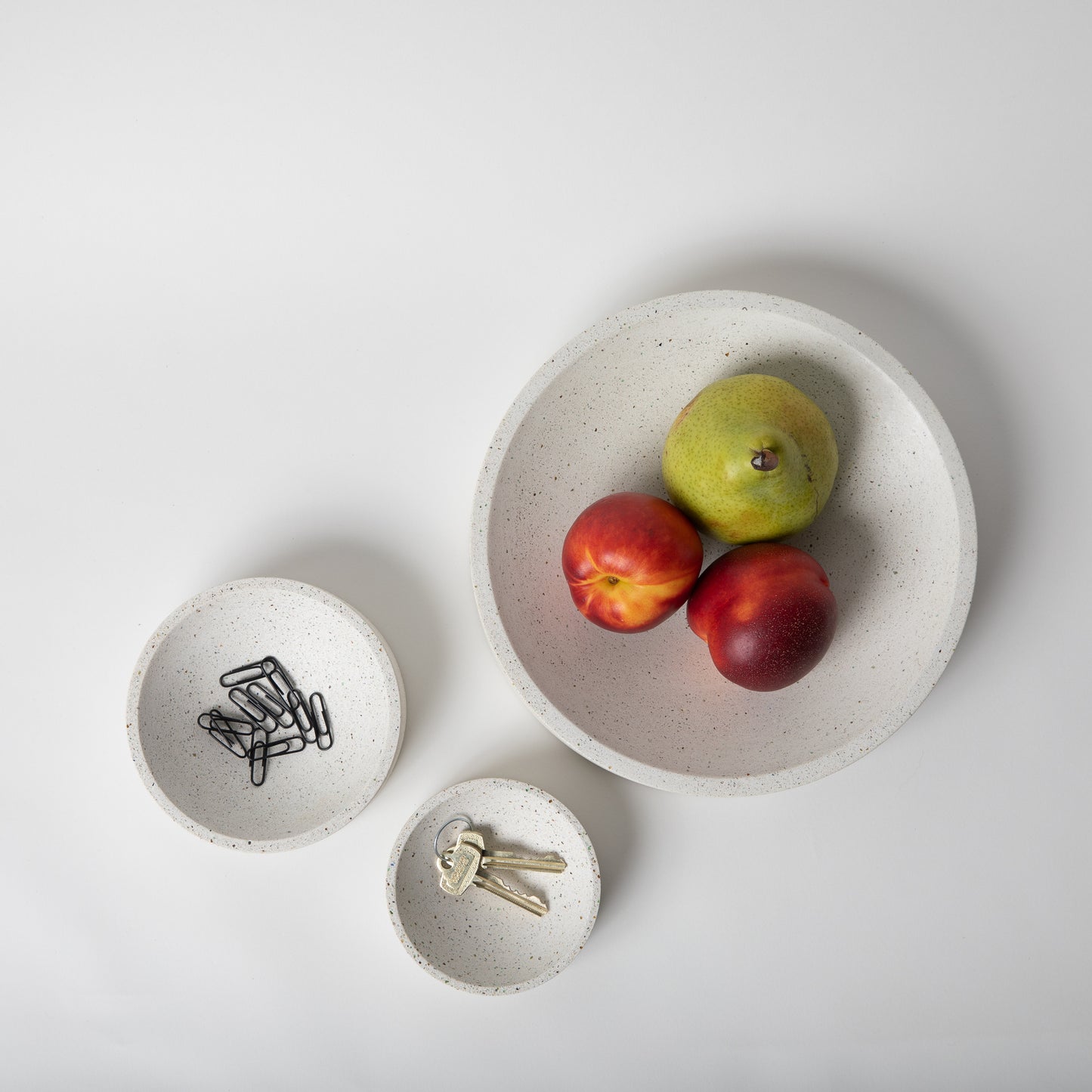 Large concrete centerpiece bowl in white terrazzo holding fruit next to other sizes for scale.