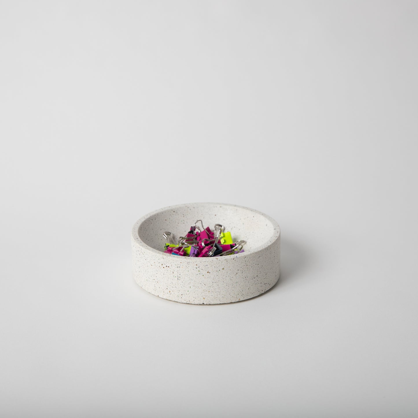 5 inch terrazzo concrete catch all with cork base in white with paper clips in it.