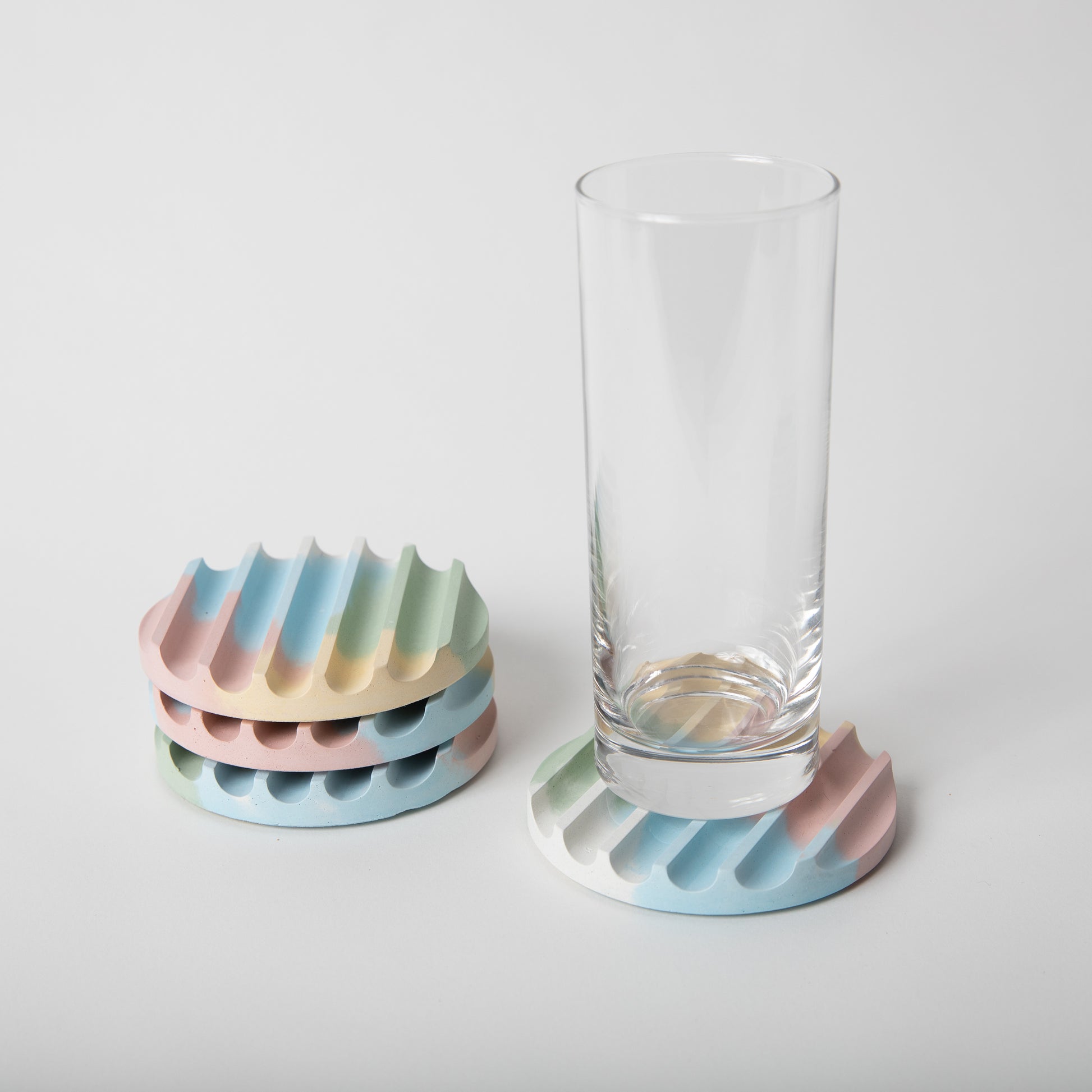 Concrete coaster set with cork base in jawbreaker (multicolor) shown with glass.