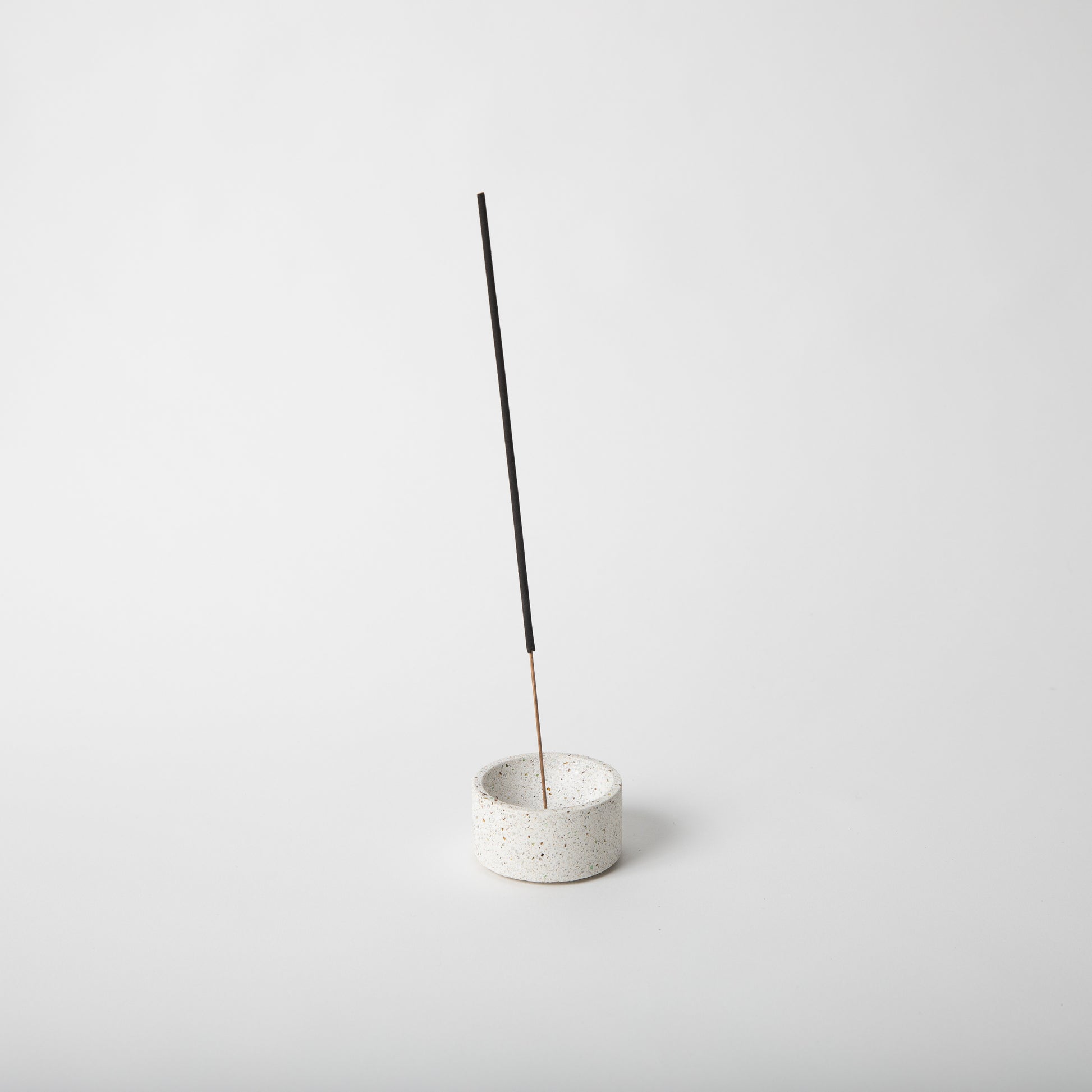 Round terrazzo concrete incense holder in white with an incense stick.