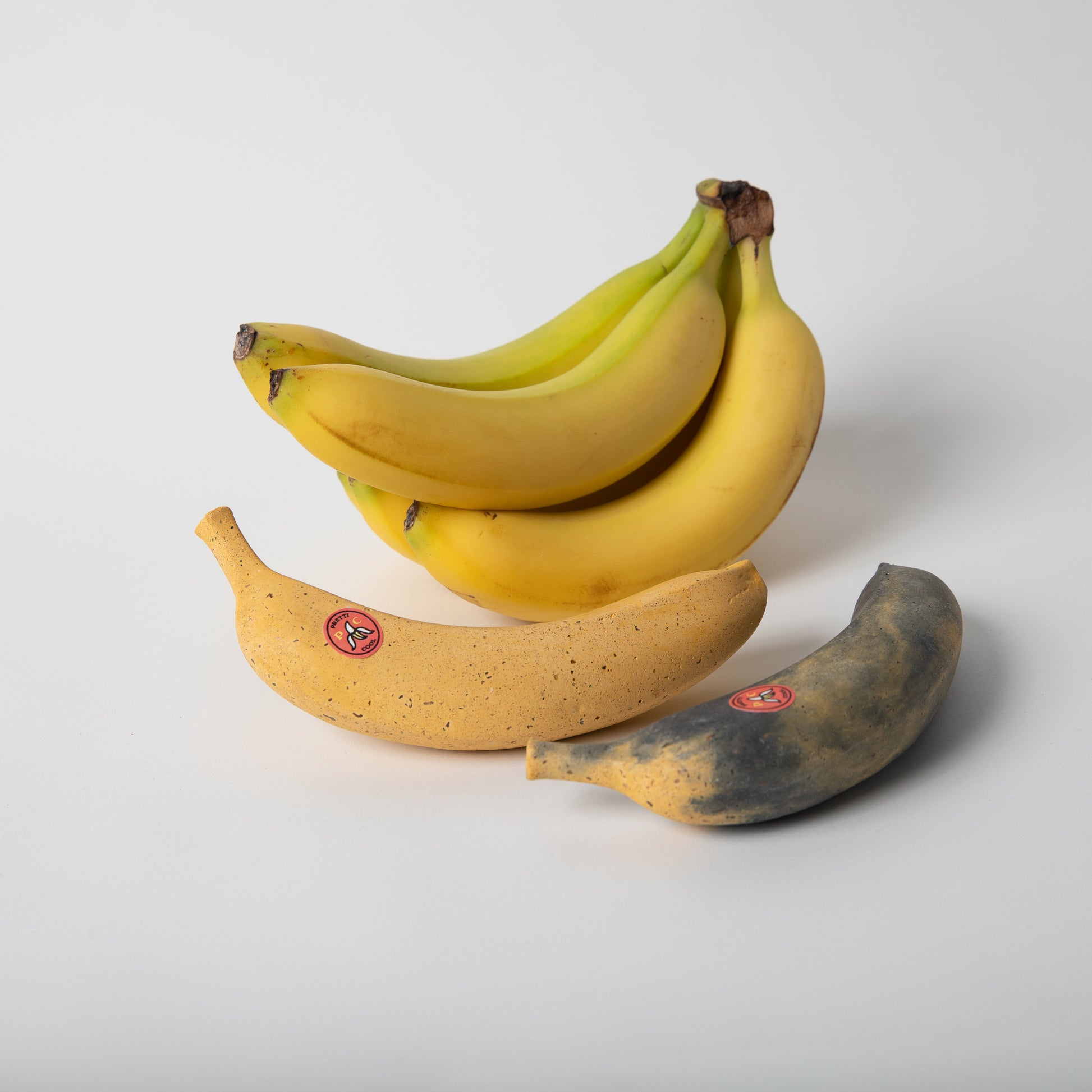 Concrete banana in both styles, banana bread (overly ripe color) and perfectly ripe next to bunch of real bananas.