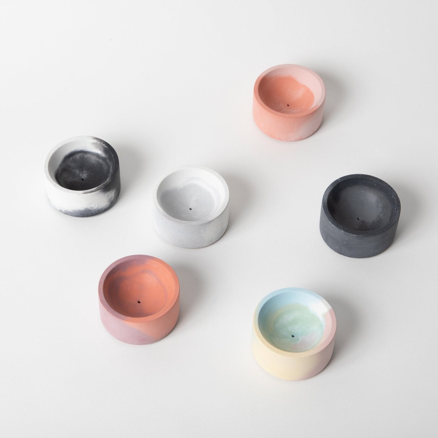 Round concrete incense holder in various colors arranged.