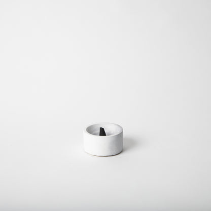 Round concrete incense holder in grey and white with an incense cone.