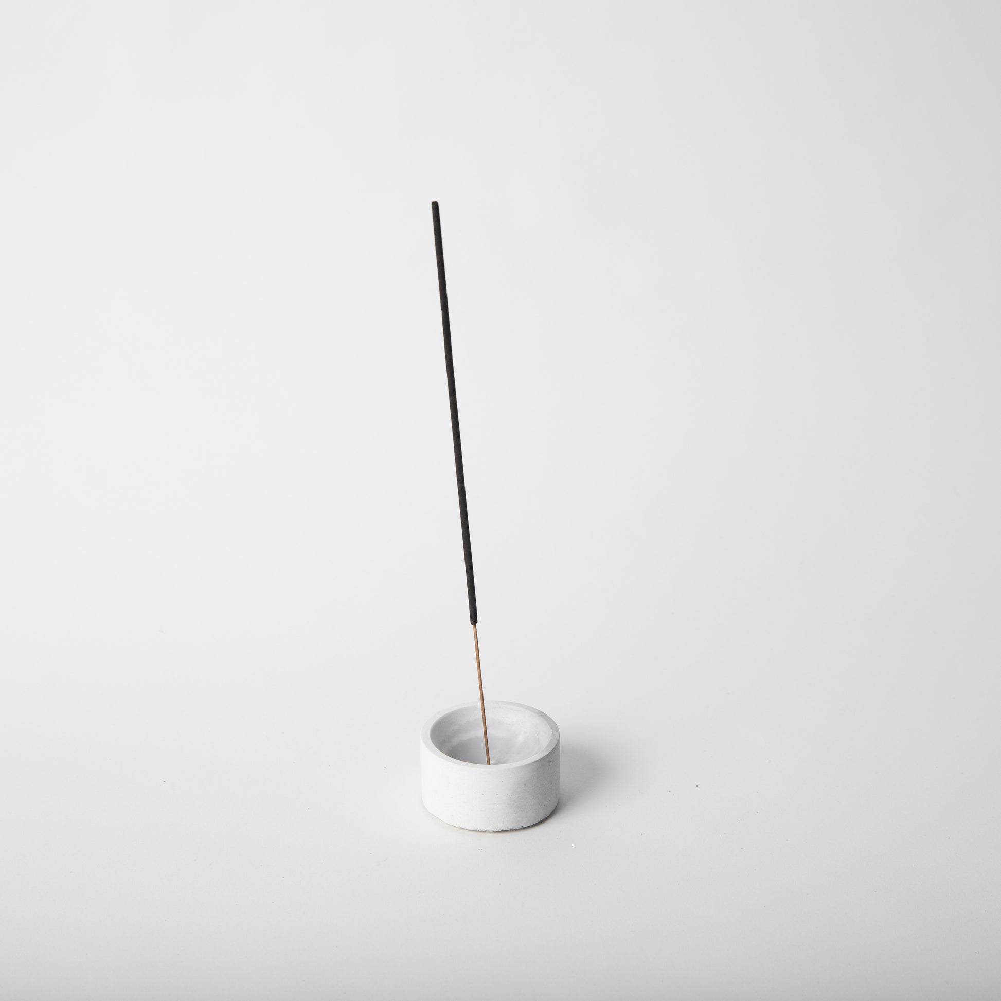 Round concrete incense holder in grey and white with an incense stick.