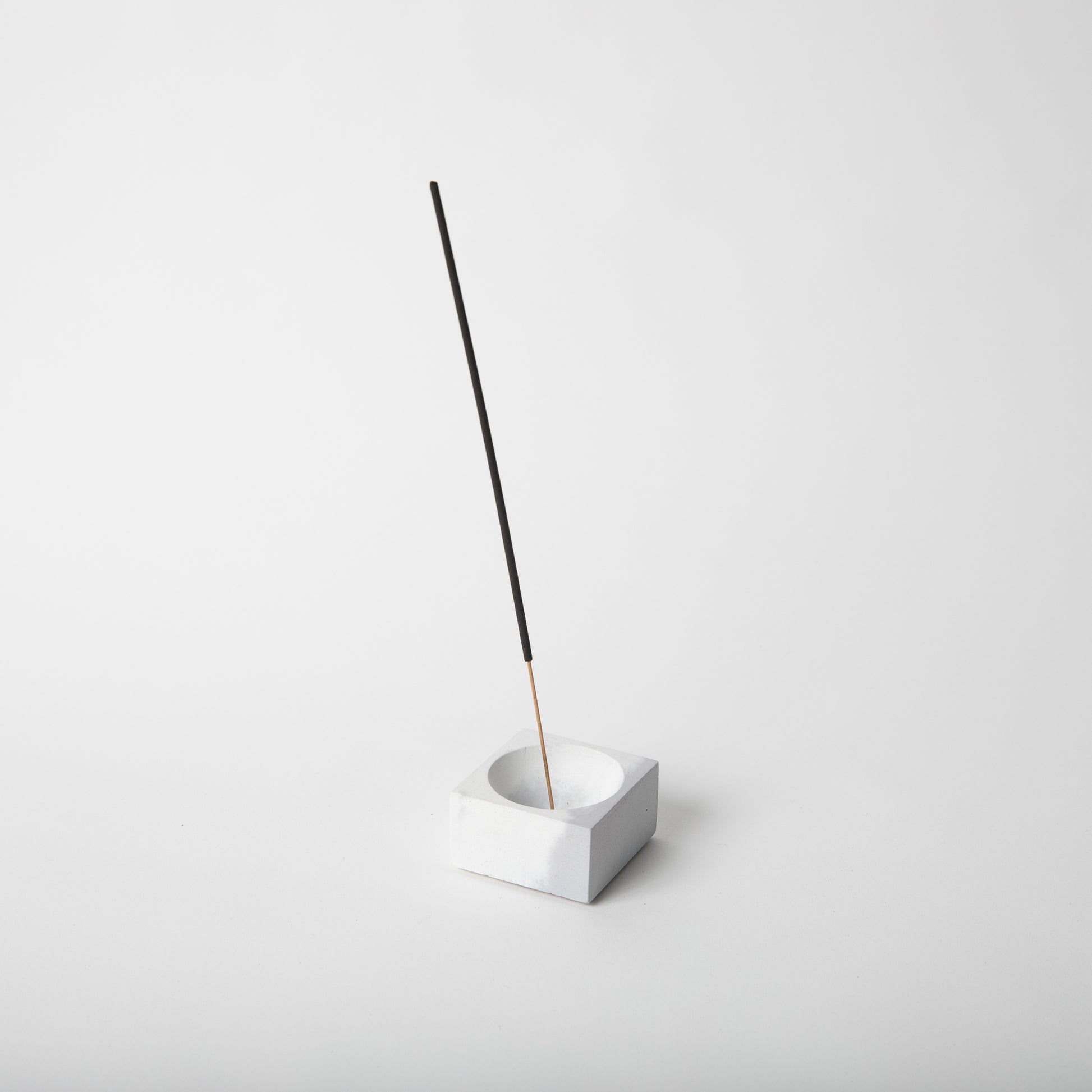 Square concrete incense holder in grey and white with incense stick.