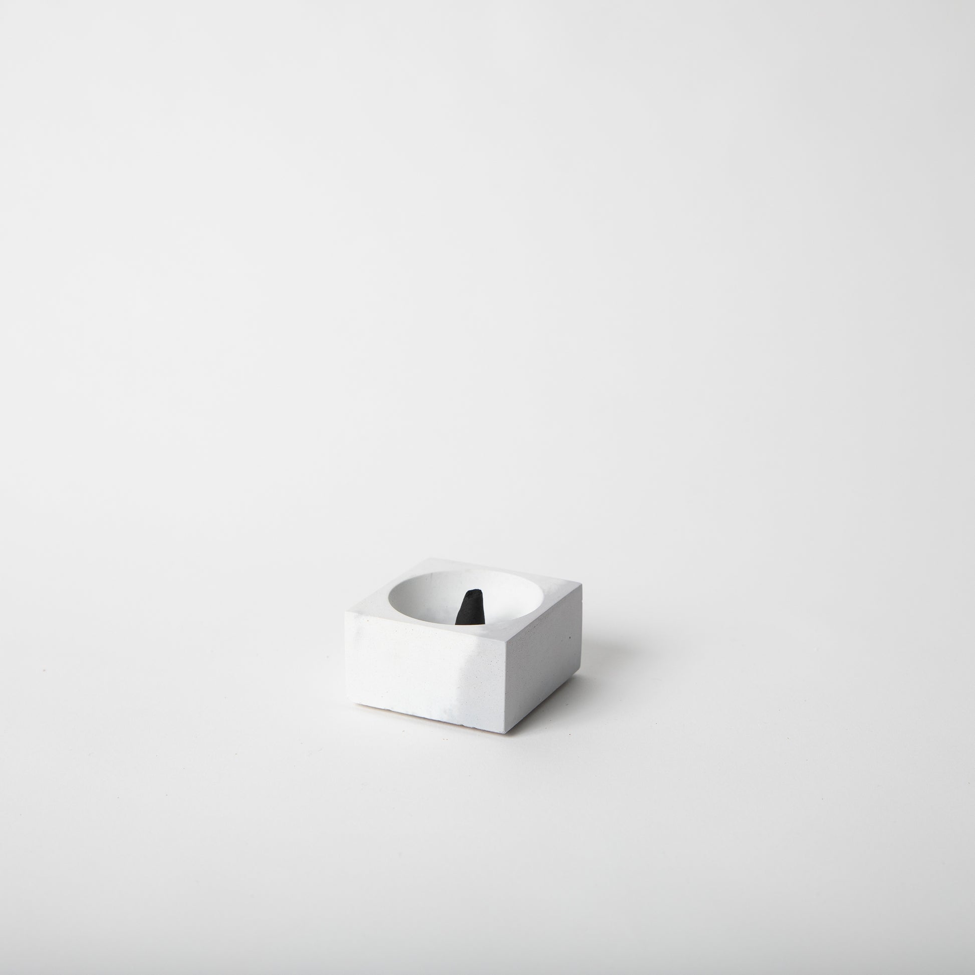 Square concrete incense holder in grey and white with incense cone.