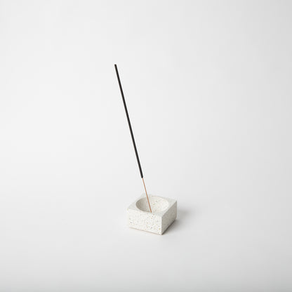 Square concrete terrazzo incense holder in white with incense stick.