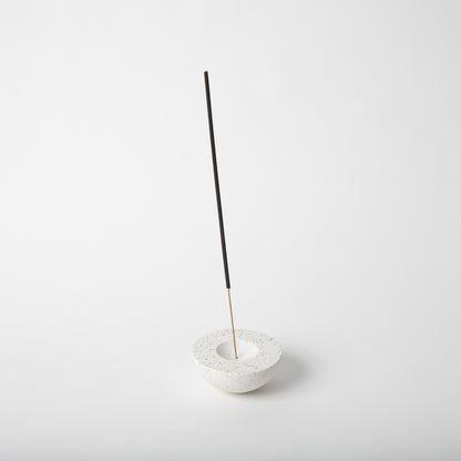 Half sphere shaped incense holder in white terrazzo. Shown holding incense stick.