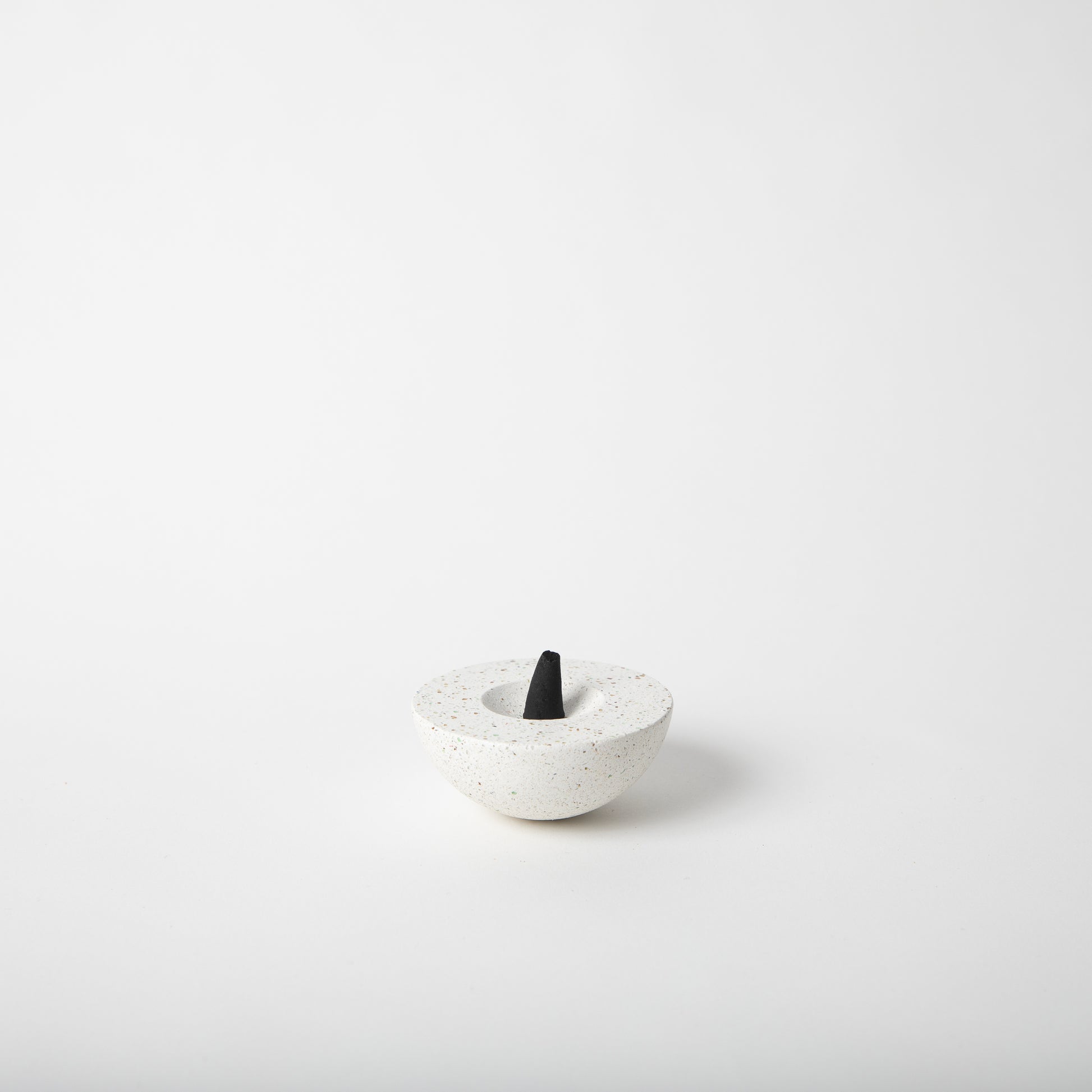 Half sphere shaped incense holder in white terrazzo. Shown holding incense cone.
