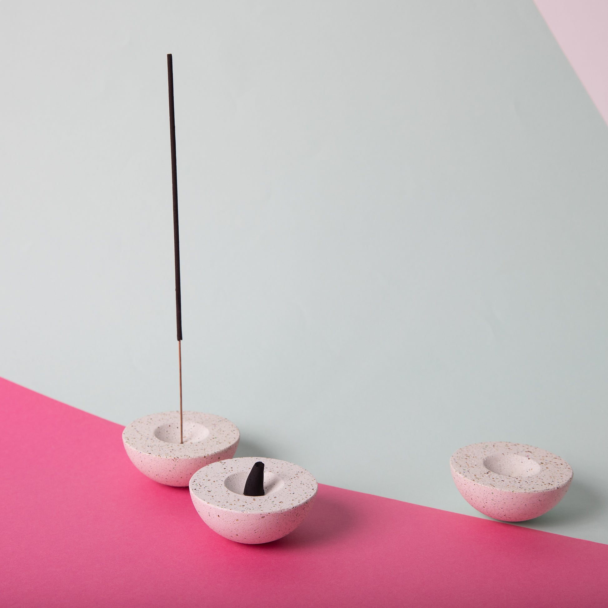 Half sphere shaped incense holder in white terrazzo. Shown holding incense.