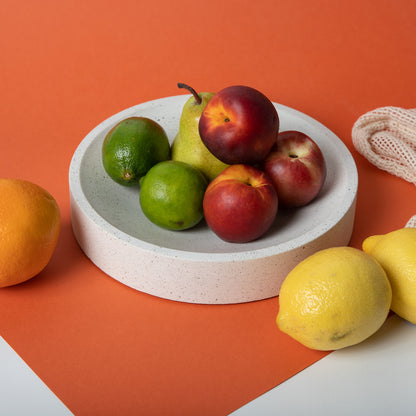 Large concrete centerpiece bowl in white terrazzo holding fruit on colorful backdrop.