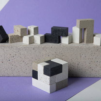 Concrete soma cube desk puzzle put together in front of the various 7 pieces.